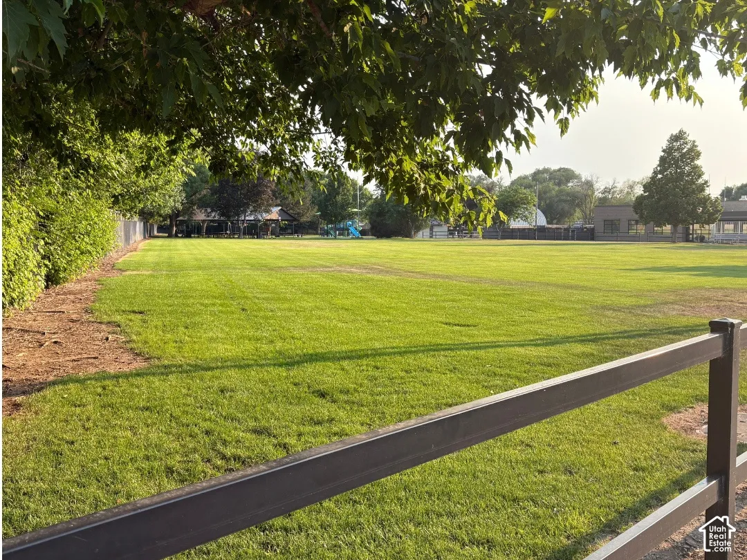 At park next door, Expansive green space featuring a wood-finish fence, mature trees, and natural landscaping