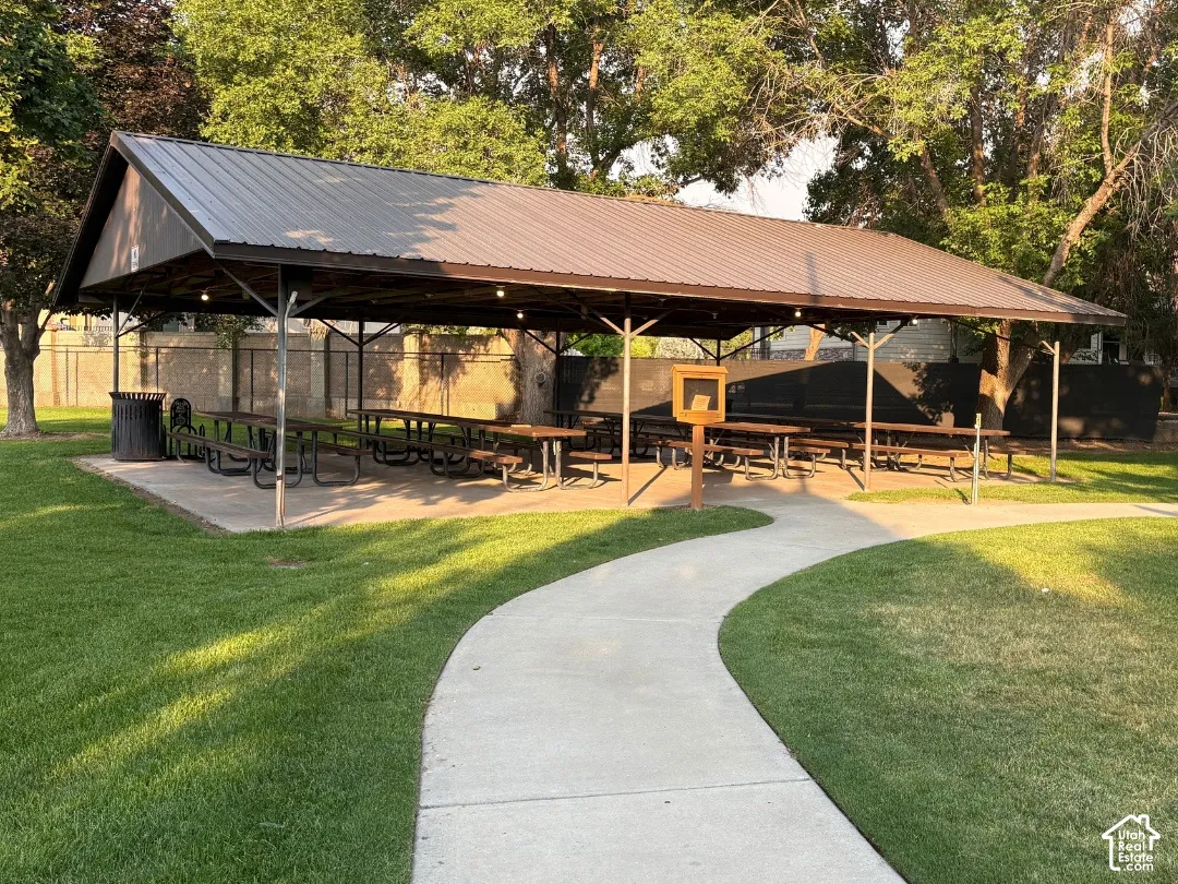 Spacious covered picnic area at park next door featuring a metal roof, concrete pad, string lighting, and extensive green space