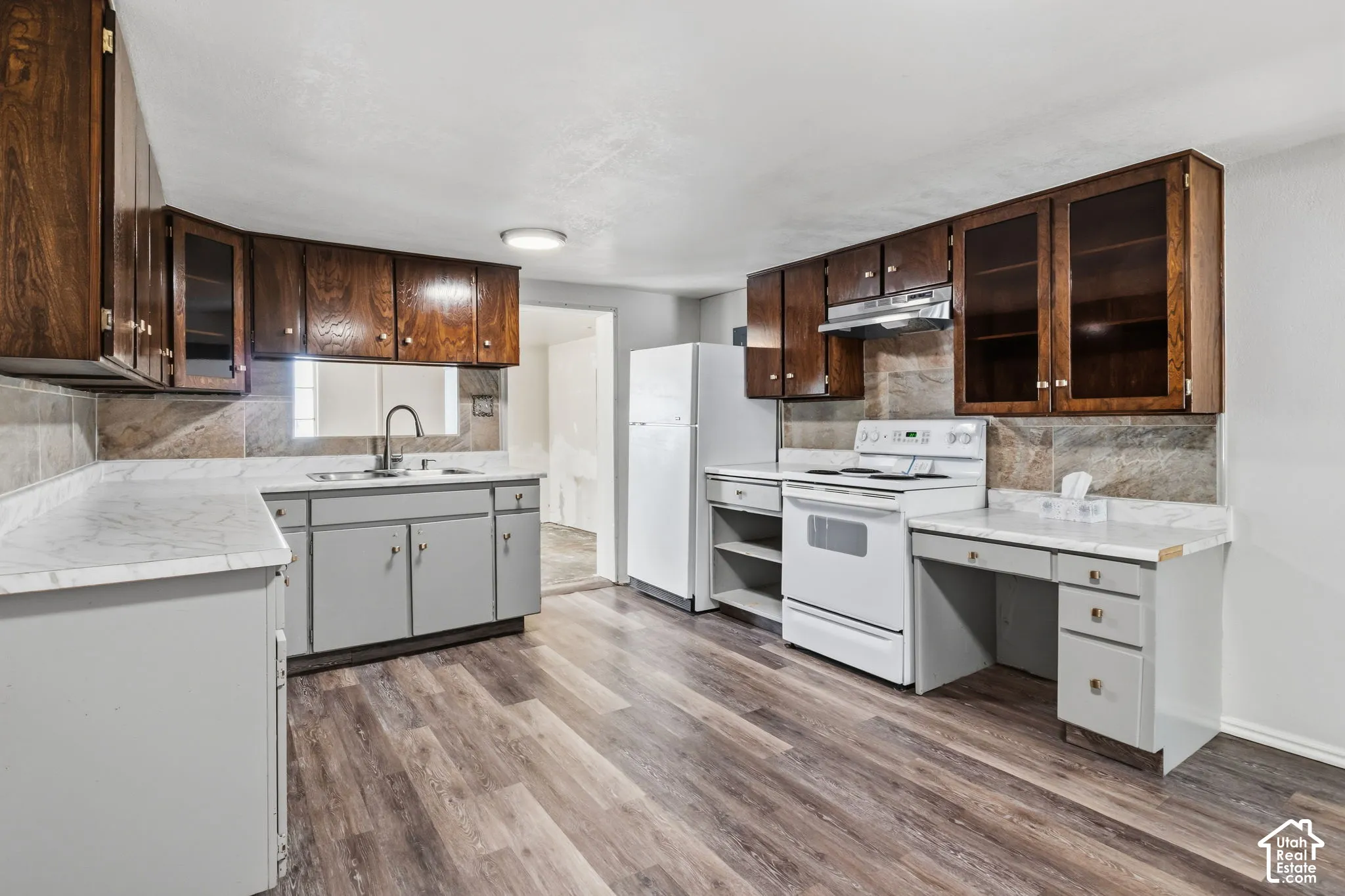 Kitchen featuring laminate flooring, wood cabinetry with glass-front uppers, light-toned countertops, and white electric stove, built in desk
