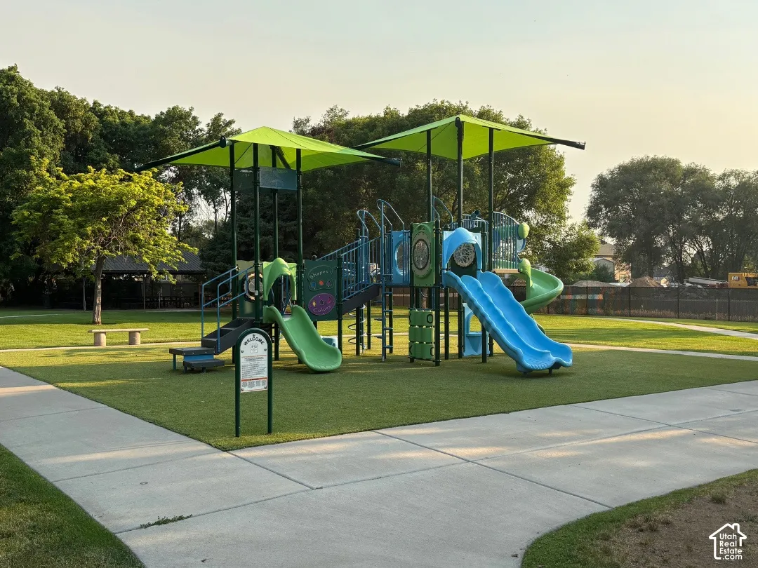 Community playground next door with multiple slides and climbing structures, artificial turf surfacing, and surrounding mature trees