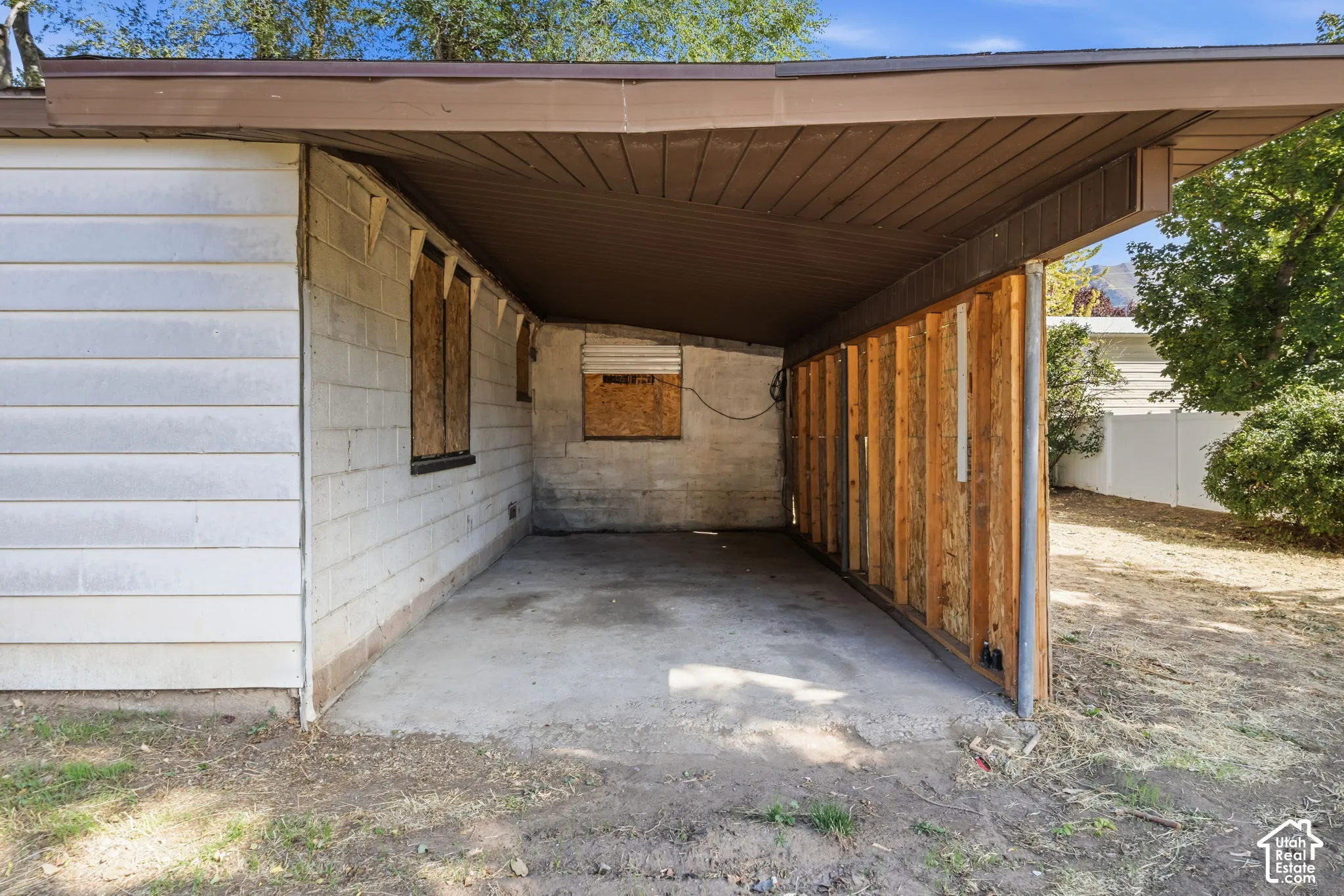 Covered carport with a concrete slab, metal-paneled ceiling, and exposed wood over metal posts