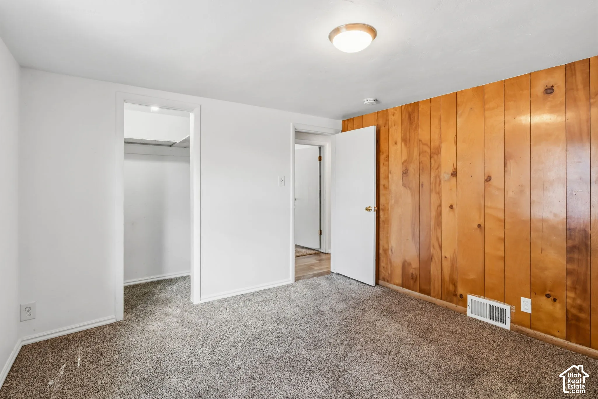 Textured carpeting, wood panel accent wall, white painted walls, white trim, and a flush mount ceiling light fixture