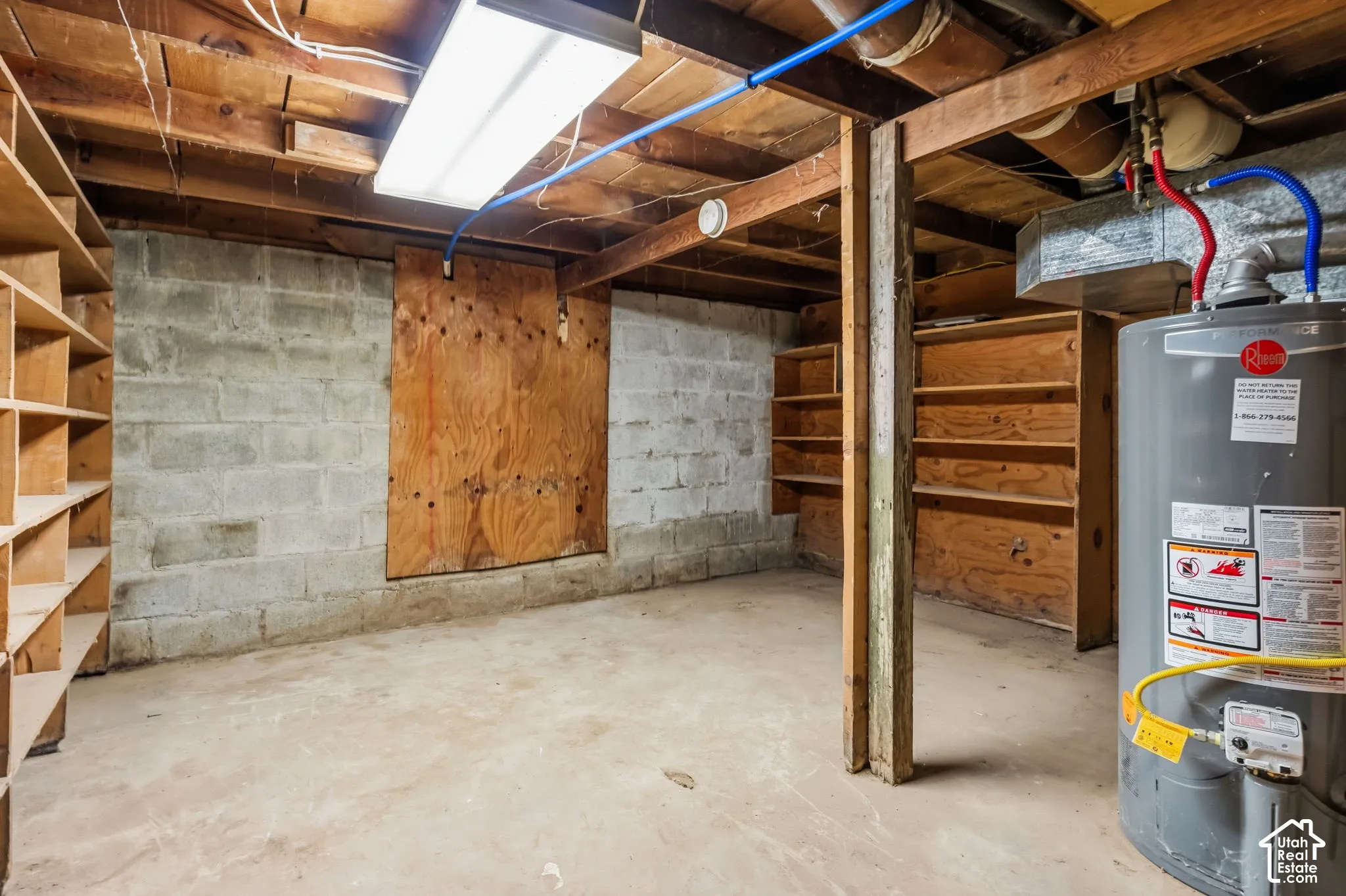 Basement storage and crawl space. Concrete flooring with concrete block walls, exposed wood ceiling beams, built-in wooden shelving, and a Rheem water heater