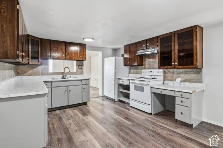 Kitchen featuring laminate flooring, wood cabinetry with glass-front uppers, light-toned countertops, and white electric stove, built in desk