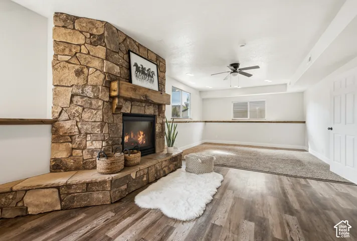 Stone-clad fireplace with a wood mantel, wood-finish flooring, recessed lighting, and a ceiling fan