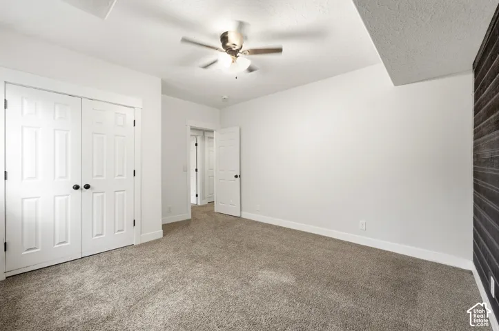 Carpeted flooring, white walls, ceiling fan with integrated lighting, paneled bifold closet doors, and a wood-slat accent wall