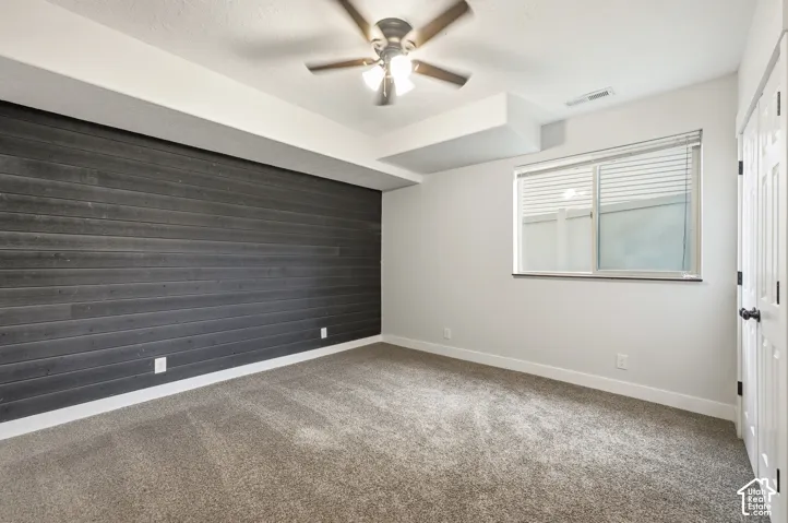 Accent wall featuring dark wood-finish paneling, light-colored carpeting, white baseboards, a ceiling fan, and a window with blinds