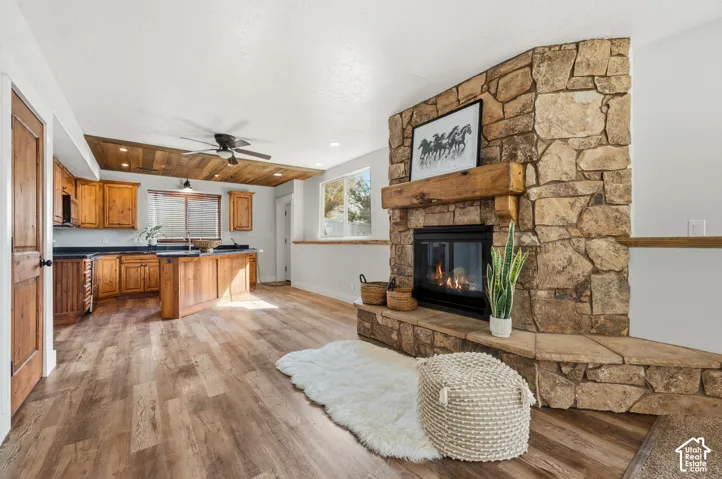 Stone-clad corner fireplace with a substantial wood mantel, wood-finish flooring, wood-paneled ceiling with recessed lighting, and kitchen cabinetry with a dark countertop