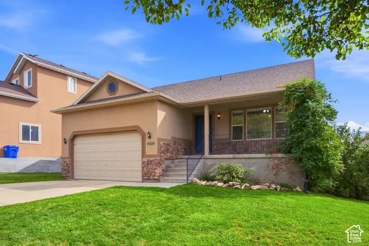 Stucco exterior with stone accents, covered front porch, integrated garage, concrete driveway, and a front lawn