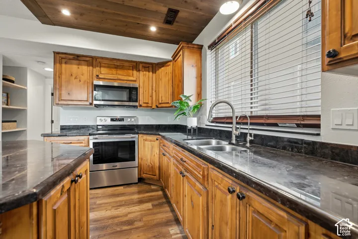 Kitchen featuring wood-finish cabinetry, dark countertops, stainless steel appliances, and a wood-paneled ceiling accent