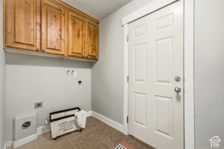 Wood-finish upper cabinetry, light gray wall paint, and a paneled white door with metal hardware, over beige tile flooring