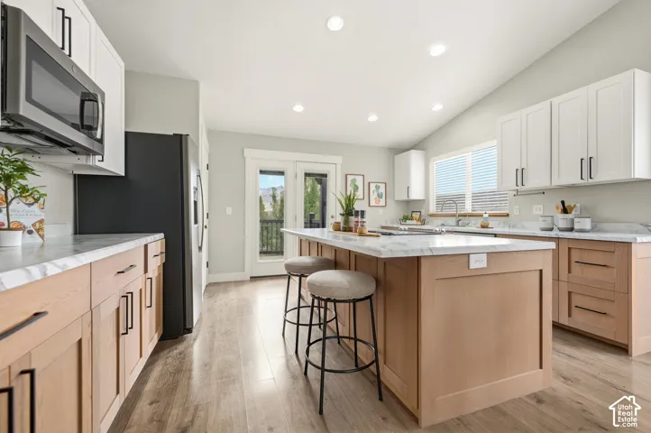 Kitchen featuring wood-finish flooring, two-tone cabinetry, a central island with seating, a stainless steel microwave, and white countertops