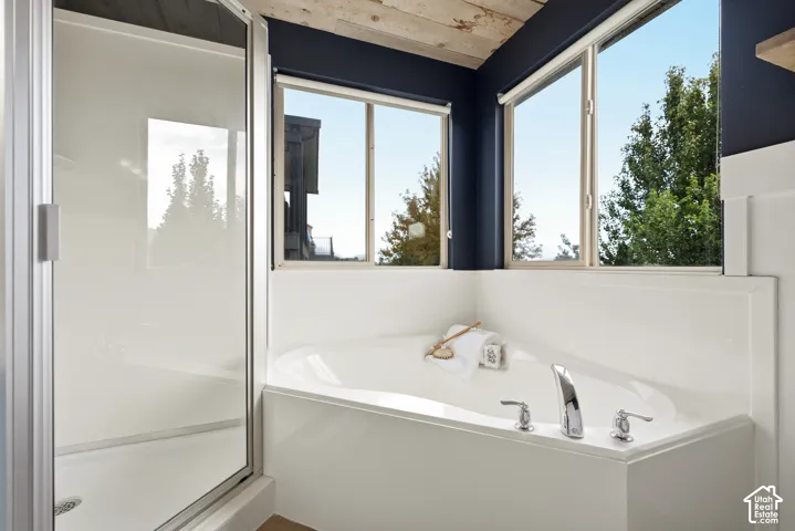 Built-in soaking tub with deck-mounted fixtures, separate shower enclosure with clear glass, and natural wood-finish ceiling