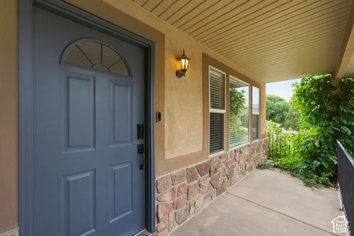Covered porch with concrete flooring, stone facade, stucco exterior, and a dark paneled entry door with an arched transom
