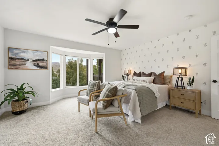 Bay window with multiple panes, ceiling fan with integrated lighting, patterned accent wall, and carpet flooring