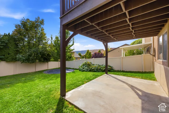 Covered concrete patio with overhead deck structure, expansive lawn, and partial privacy fencing
