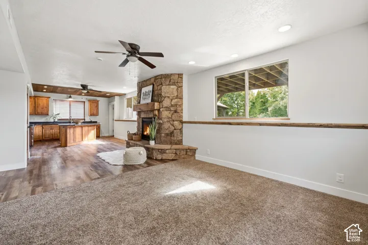 Stone-clad fireplace with a wood mantel, wood-finish flooring, recessed lighting, and a ceiling fan