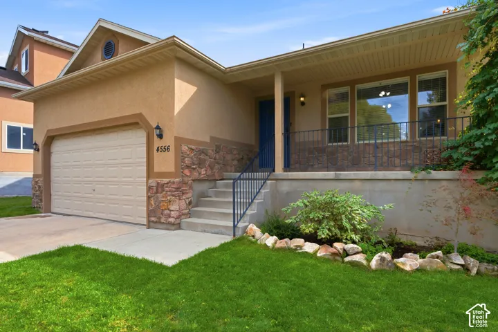 Stucco exterior with stone accents, covered front porch, integrated two-car garage, and mature landscaping