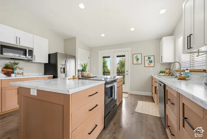 Kitchen featuring wood-finish flooring, two-tone cabinetry, stainless steel appliances, a center island with a stone-finish countertop, and double glass-panel doors