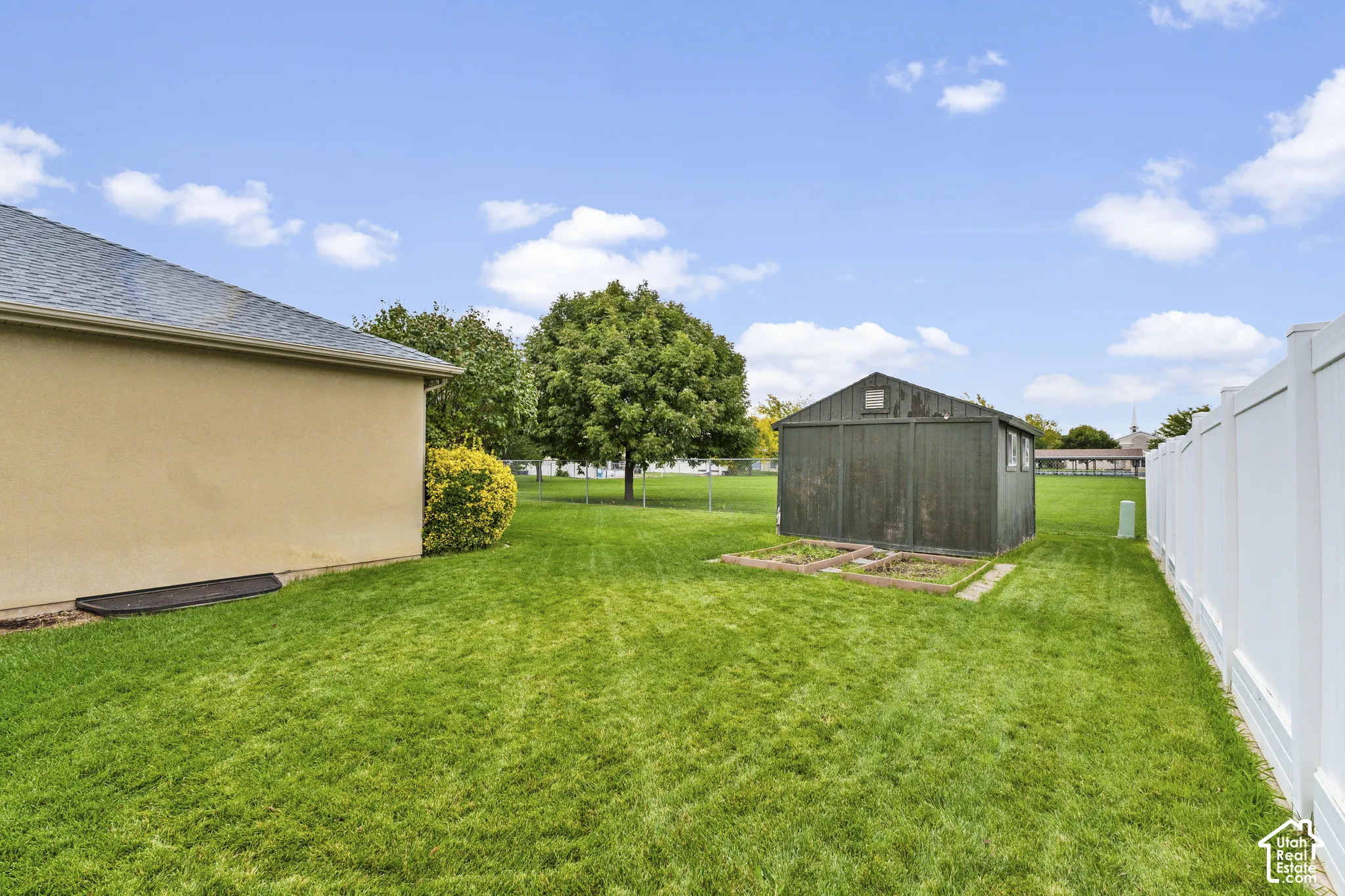 Expansive grassy yard featuring a privacy fence, mature trees, and a storage shed