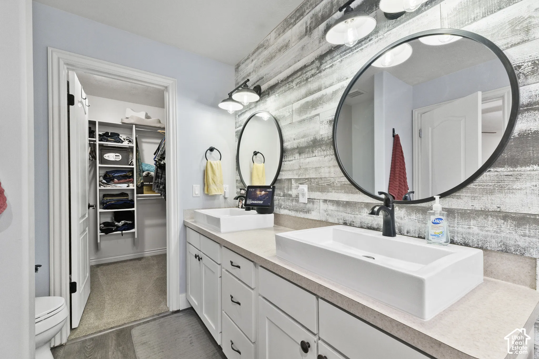 Updated Master Bathroom with dual vessel sinks, expansive vanity with white cabinetry, wood-finish accent wall, and walk-in closet with built-in shelving