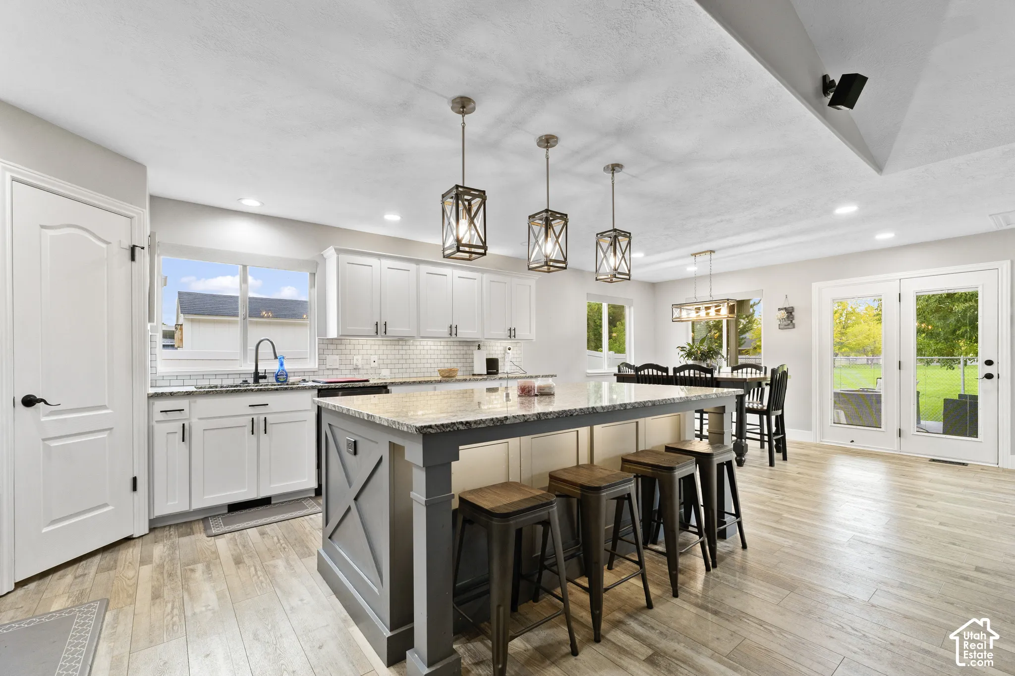 Updated Kitchen featuring a large central island with seating, white shaker cabinetry, light-toned wood-finish flooring, and dual glass panel doors