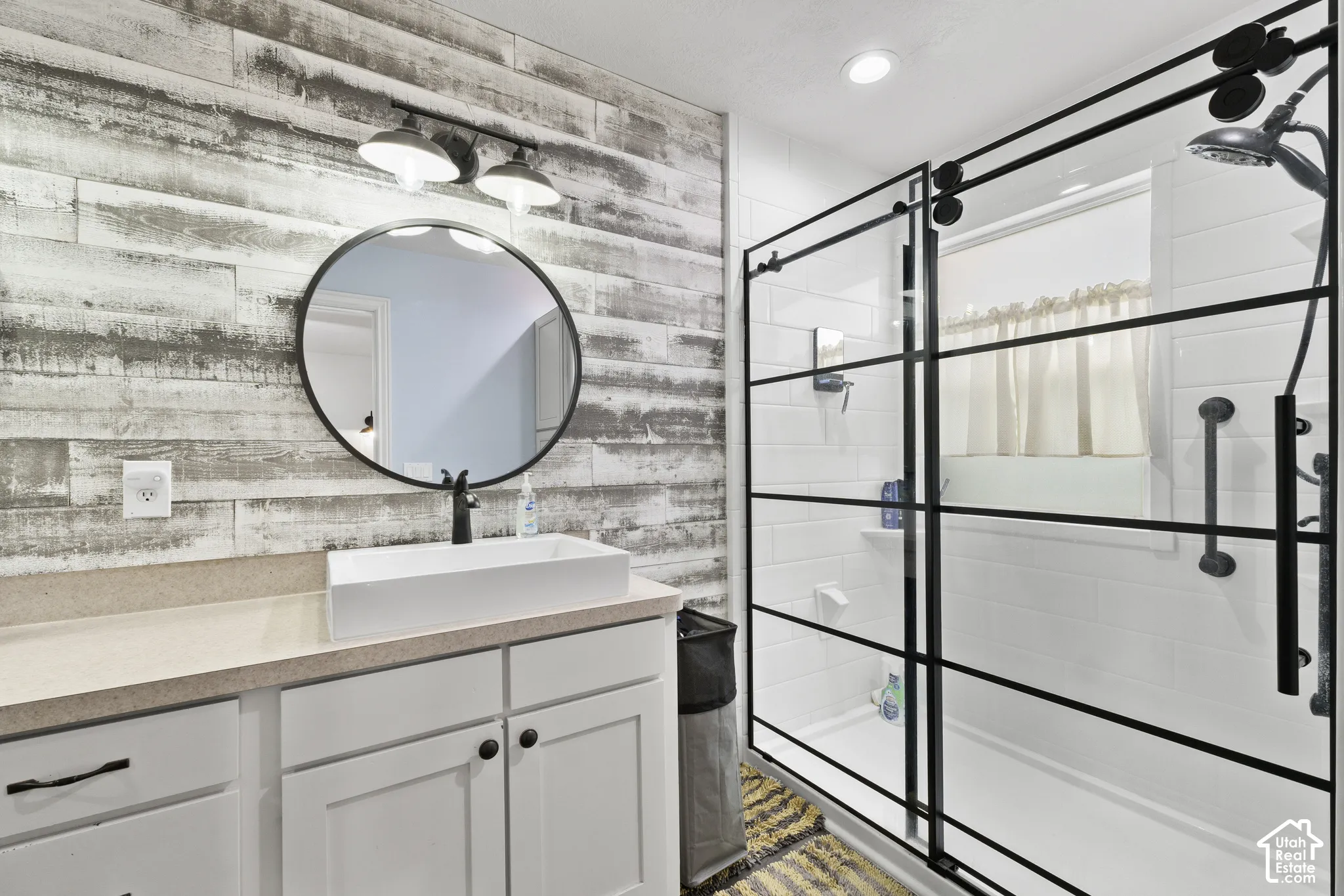 Updated Master Bathroom featuring distressed wood-finish accent wall with a circular mirror and large shower.