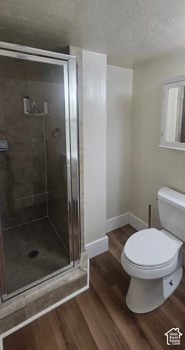Shower enclosure with glass door and tile surround, complemented by wood-finish flooring and a wall-mounted medicine cabinet