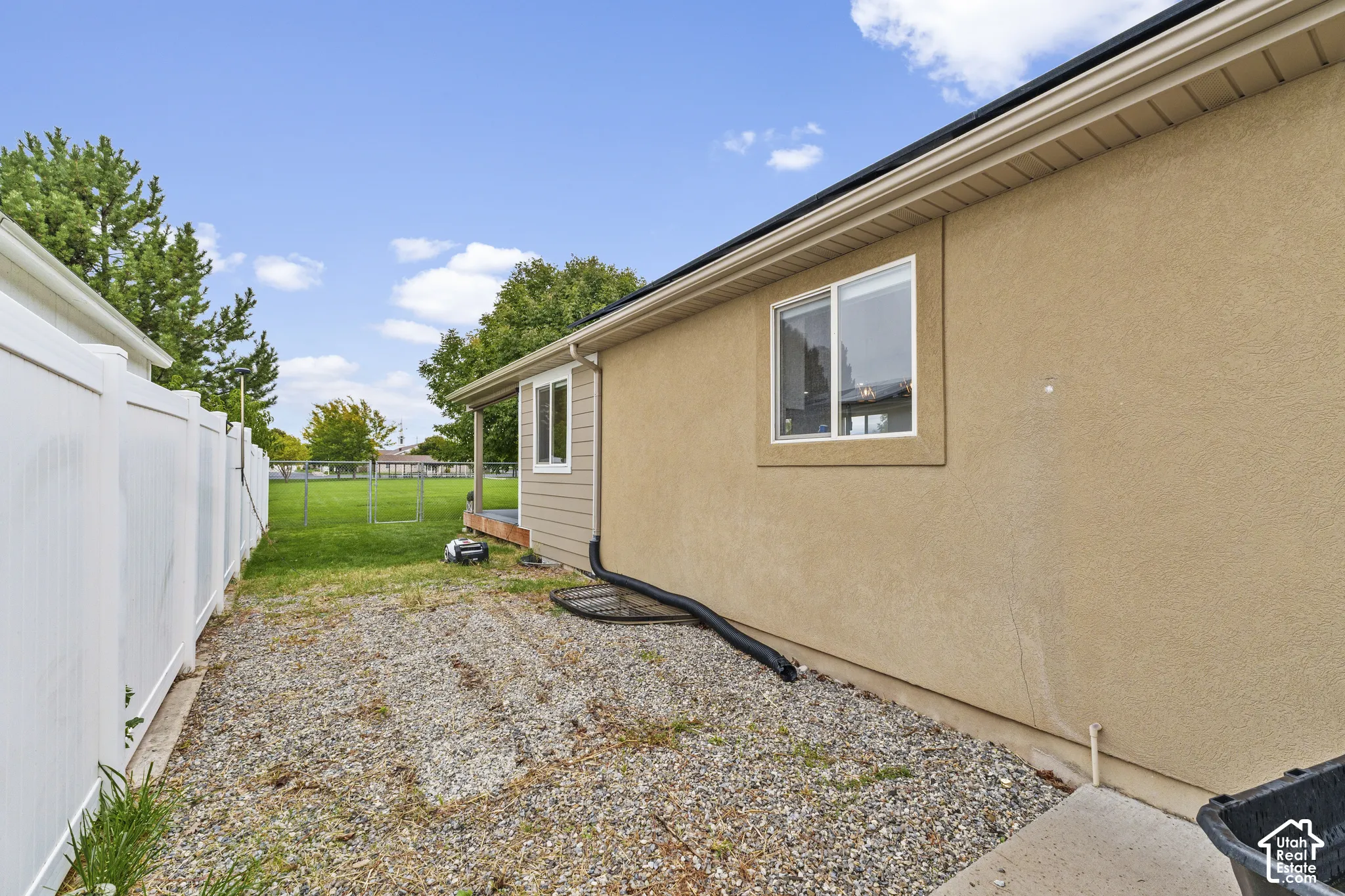 Stucco exterior with white-framed windows, white vinyl fencing, and a gravel walkway