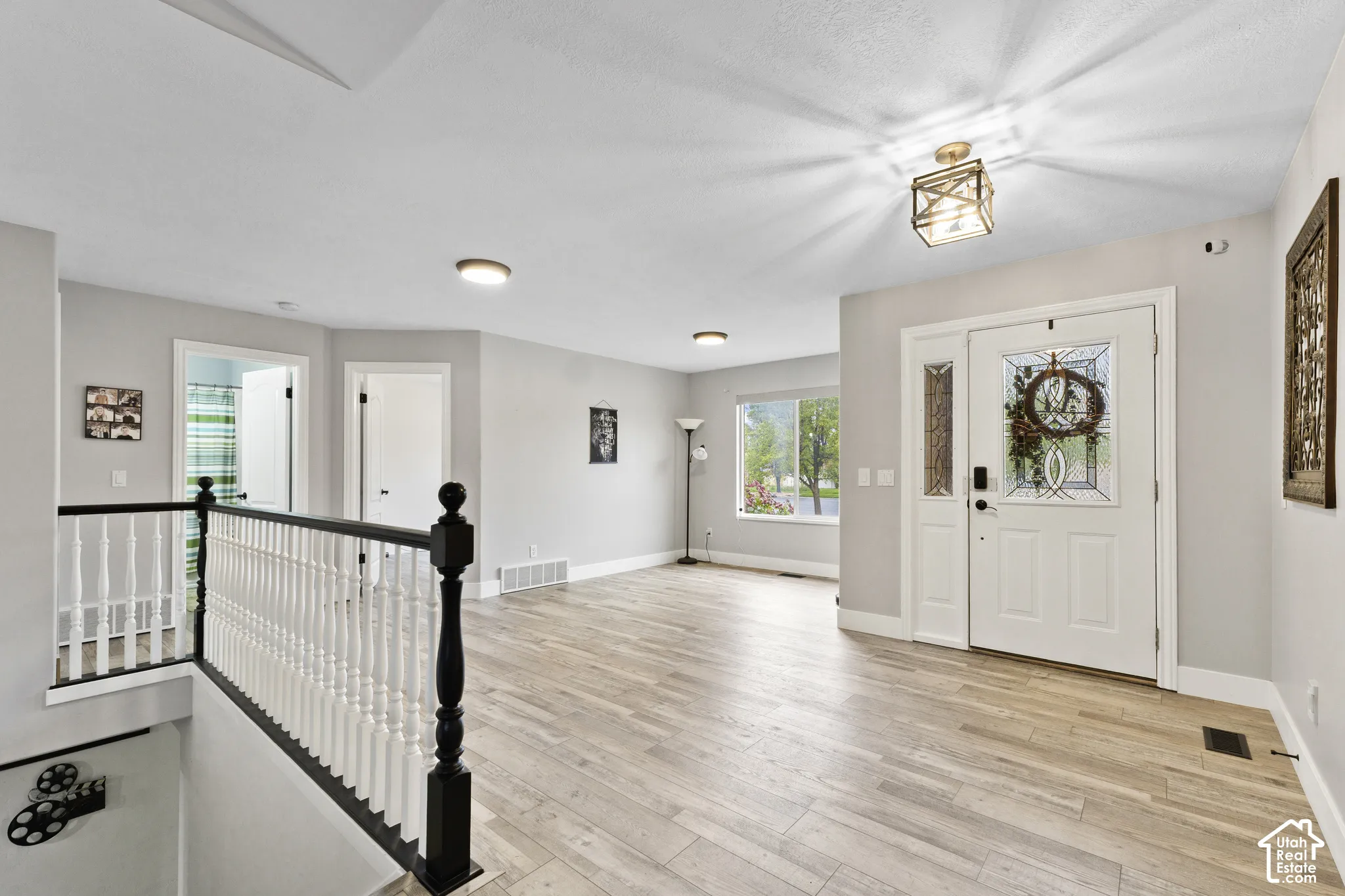 Entryway featuring light wood-finish flooring, a white front door with decorative glass inserts, and a decorative ceiling light fixture