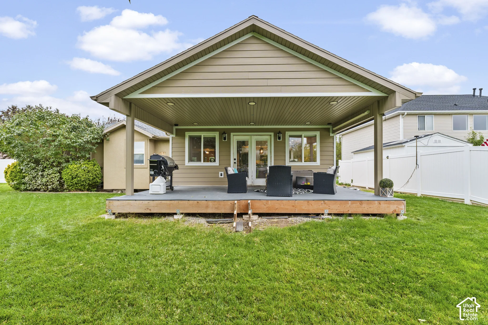 Expansive green lawn with a covered deck, durable composite decking, double glass doors, and vinyl siding