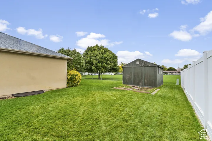 Expansive grassy yard featuring a privacy fence, mature trees, and a storage shed