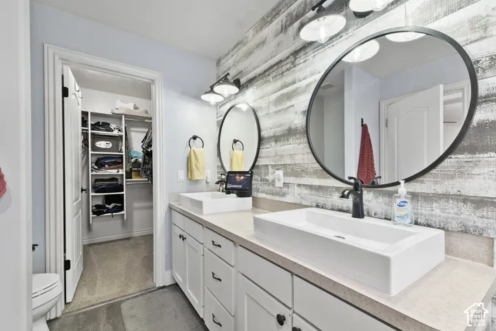 Updated Master Bathroom with dual vessel sinks, expansive vanity with white cabinetry, wood-finish accent wall, and walk-in closet with built-in shelving