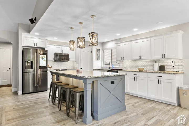 Updated Kitchen featuring a central island with a granite countertop, white shaker-style cabinetry, stainless steel appliances, a subway tile backsplash, and wood-finish flooring