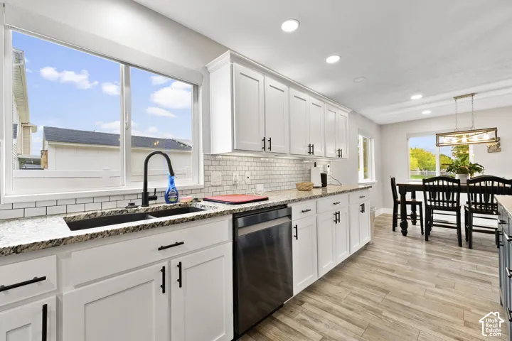 Updated Kitchen featuring white shaker cabinetry, granite countertops, white subway tile backsplash, stainless steel dishwasher, and wood-finish flooring