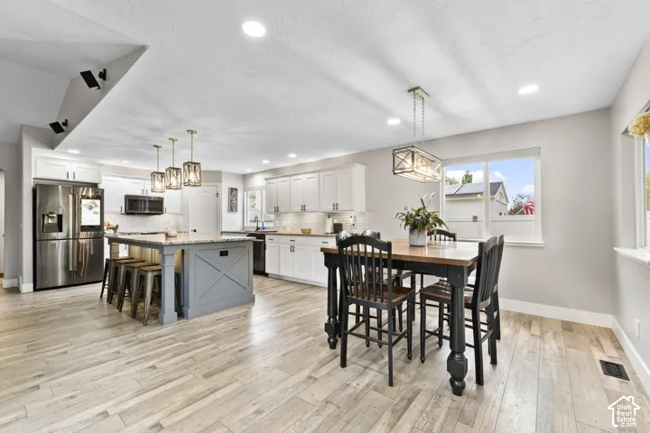 Updated Open-concept kitchen and dining area featuring wood-finish flooring, white cabinetry, a gray kitchen island with seating, and stainless steel appliances