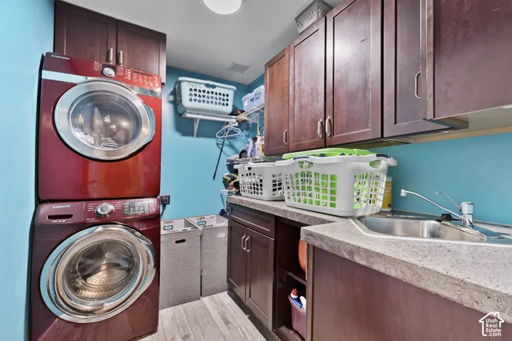 Laundry area featuring stacked appliances, overhead cabinetry, and a utility sink with a countertop