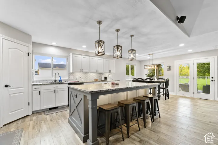 Updated Kitchen featuring a large central island with seating, white shaker cabinetry, light-toned wood-finish flooring, and dual glass panel doors