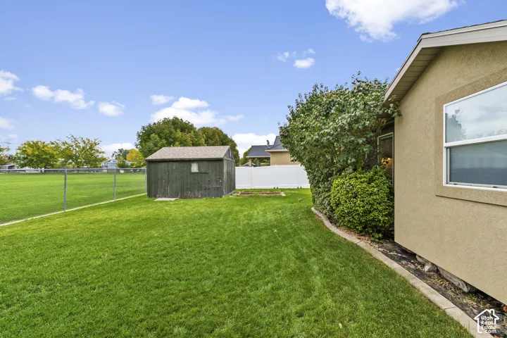 Expansive grassy yard with a storage shed, chain-link fence, and white privacy fence