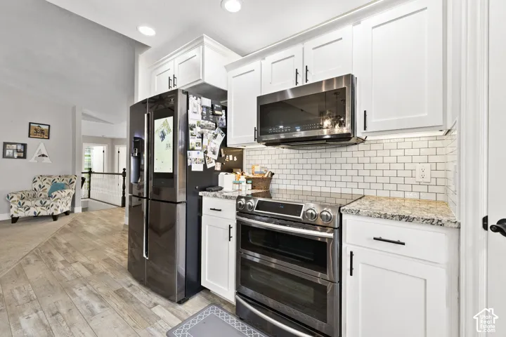 Updated Kitchen featuring white shaker cabinetry, stainless steel appliances, granite countertops, and subway tile backsplash