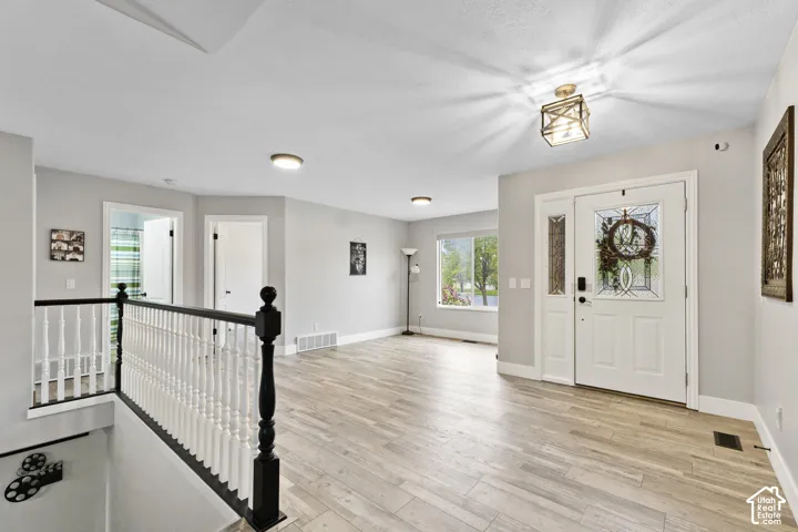 Entryway featuring light wood-finish flooring, a white front door with decorative glass inserts, and a decorative ceiling light fixture