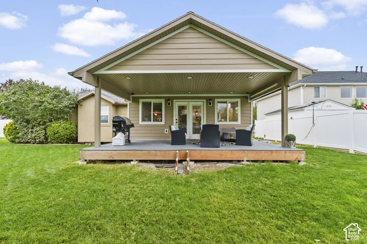 Expansive green lawn with a covered deck, durable composite decking, double glass doors, and vinyl siding