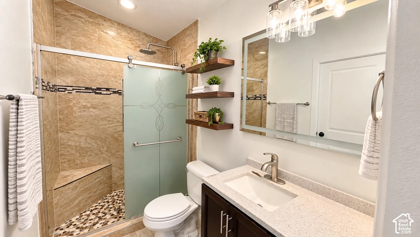 Walk-in shower with tiled walls and pebble flooring, integrated shower bench, and frosted glass sliding door