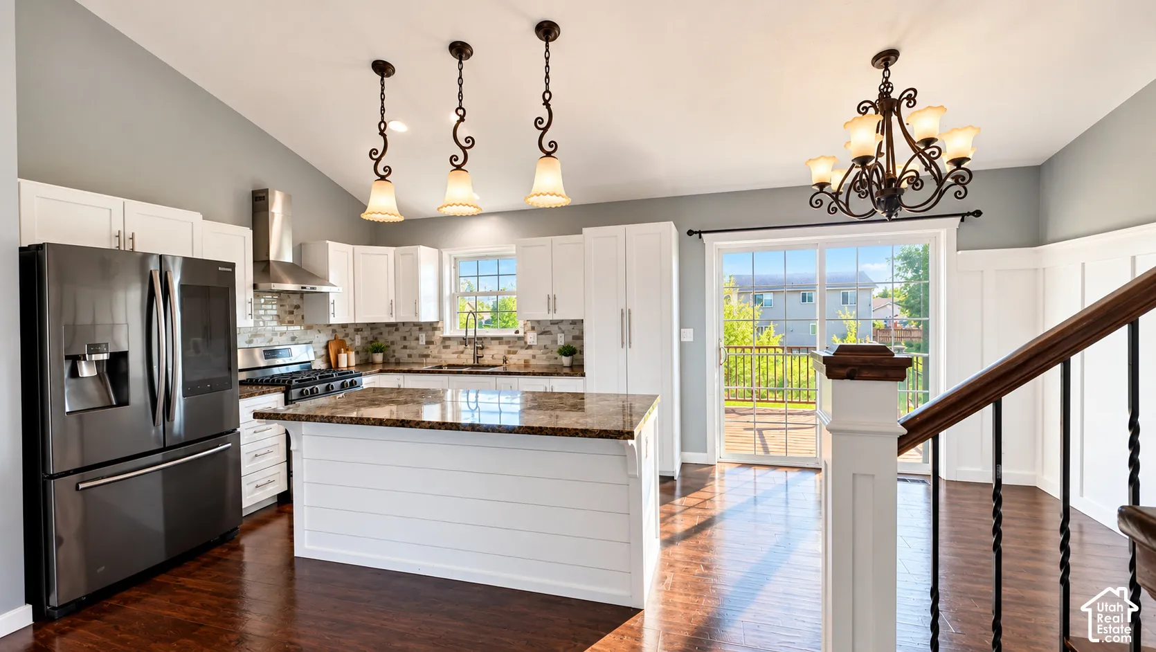 Vaulted ceiling with decorative pendant lights, white shaker cabinetry, stainless steel appliances, granite island, and wood-finish flooring