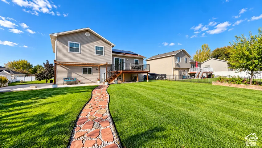 Expansive lawn with a stone pathway, two-story exterior with siding, upper-level deck, and a raised garden bed