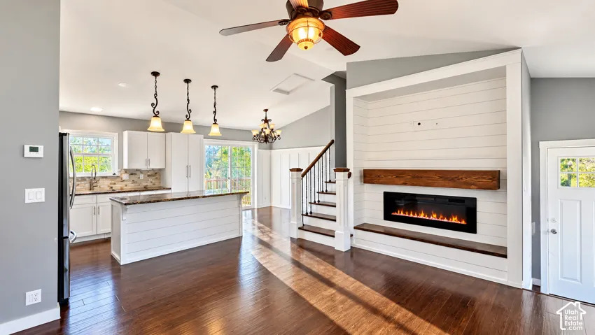 Wood-finish flooring throughout, vaulted ceiling, built-in electric fireplace with wood mantel, white shaker cabinetry, and a kitchen island with pendant lighting
