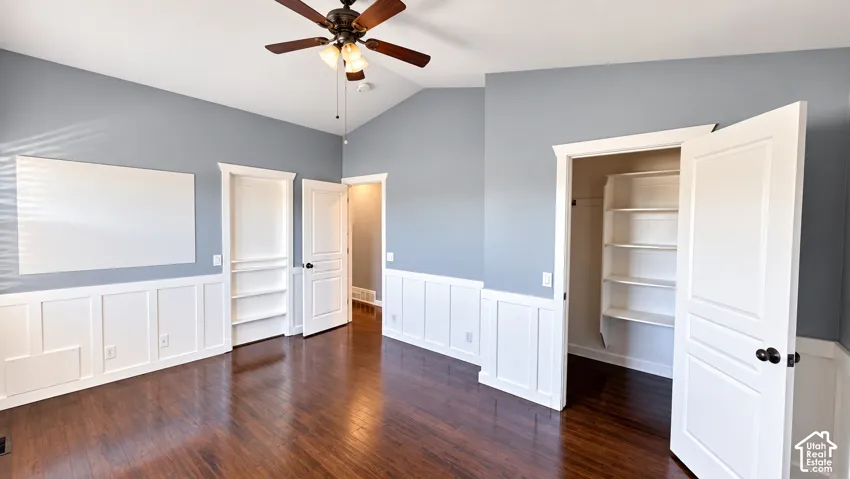 Vaulted ceiling featuring a ceiling fan, dark wood-finish flooring, wainscoting, and built-in shelving