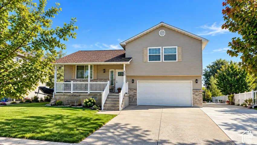 Siding exterior with stone accent, covered front porch, attached garage, concrete driveway, and front lawn