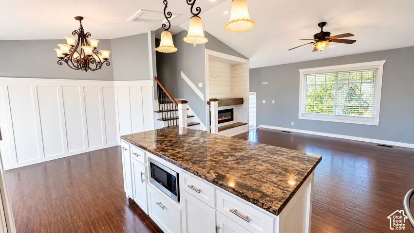 Open concept living space featuring a kitchen island with stone countertop, built-in microwave, dark wood-finish flooring, and a fireplace with a wood mantel