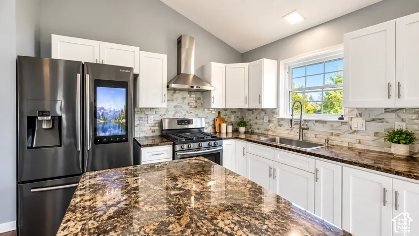Kitchen featuring white cabinetry, a stainless steel gas range, a multi-door refrigerator, a dual basin sink, and a multi-tone tile backsplash